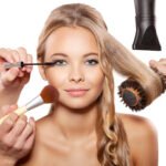 Professional makeup artist and hairdresser are preparing a fashion model. Portrait of beautiful blonde girl with blue eyes.Isolated on white background
